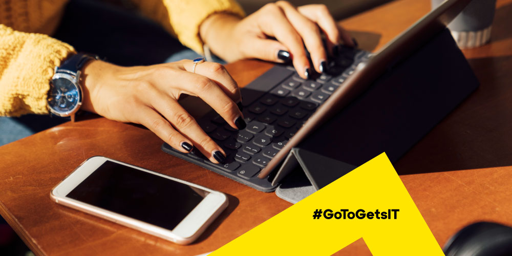 Close up of woman's hands typing on a tablet keyboard with a mobile phone nearby, showing the need to make digital workspaces work for remote work
