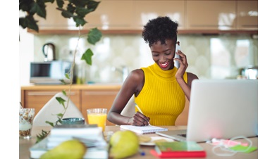 Inidvidual working remotely, sitting at kitchen table on a work call with laptop open and taking notes.
