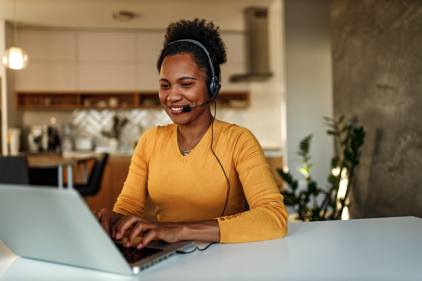 Woman wearing a headset working at a computer in her kitchen, presumably a managed service provider helping a client with an IT issue