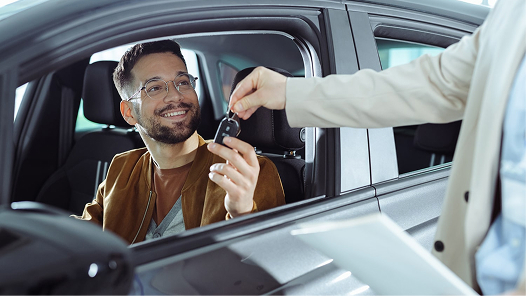 A happy customer receiving keys for his new car in a auto dealership showroom.