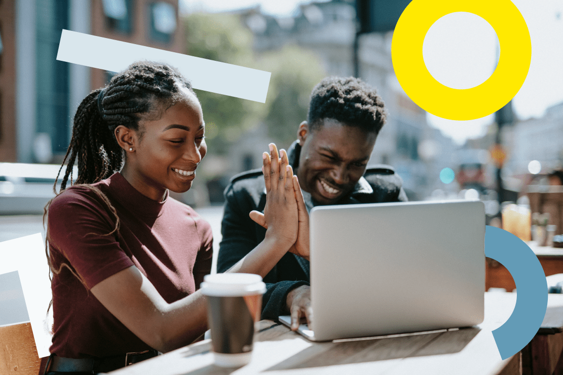 Due persone sedute all'aperto che si danno il cinque davanti a un laptop.
