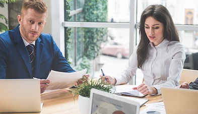 Two business professionals in a meeting with papers and laptops